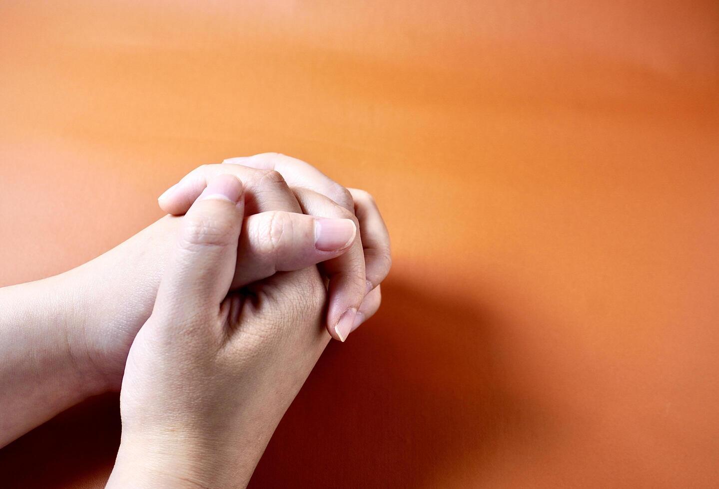 Clasped hands with praying and religious gesture pose isolated on horizontal orange brown terracotta colored background. photo