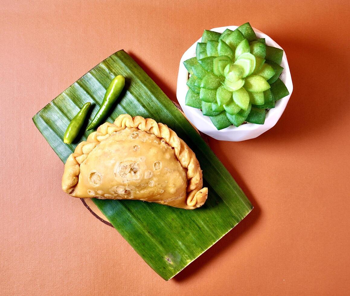Pastel sayur with green hot chilli pepper. Deep fried Indonesian jajanan pasar dessert snacks isolated on horizontal orange brown terracota background from top angle view with cactus decoration. photo