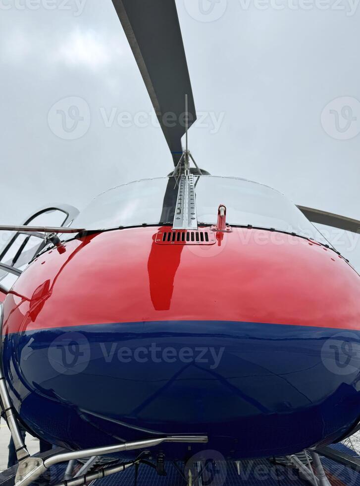Red and blue helicopter close-up with rotor blades against cloudy sky photo