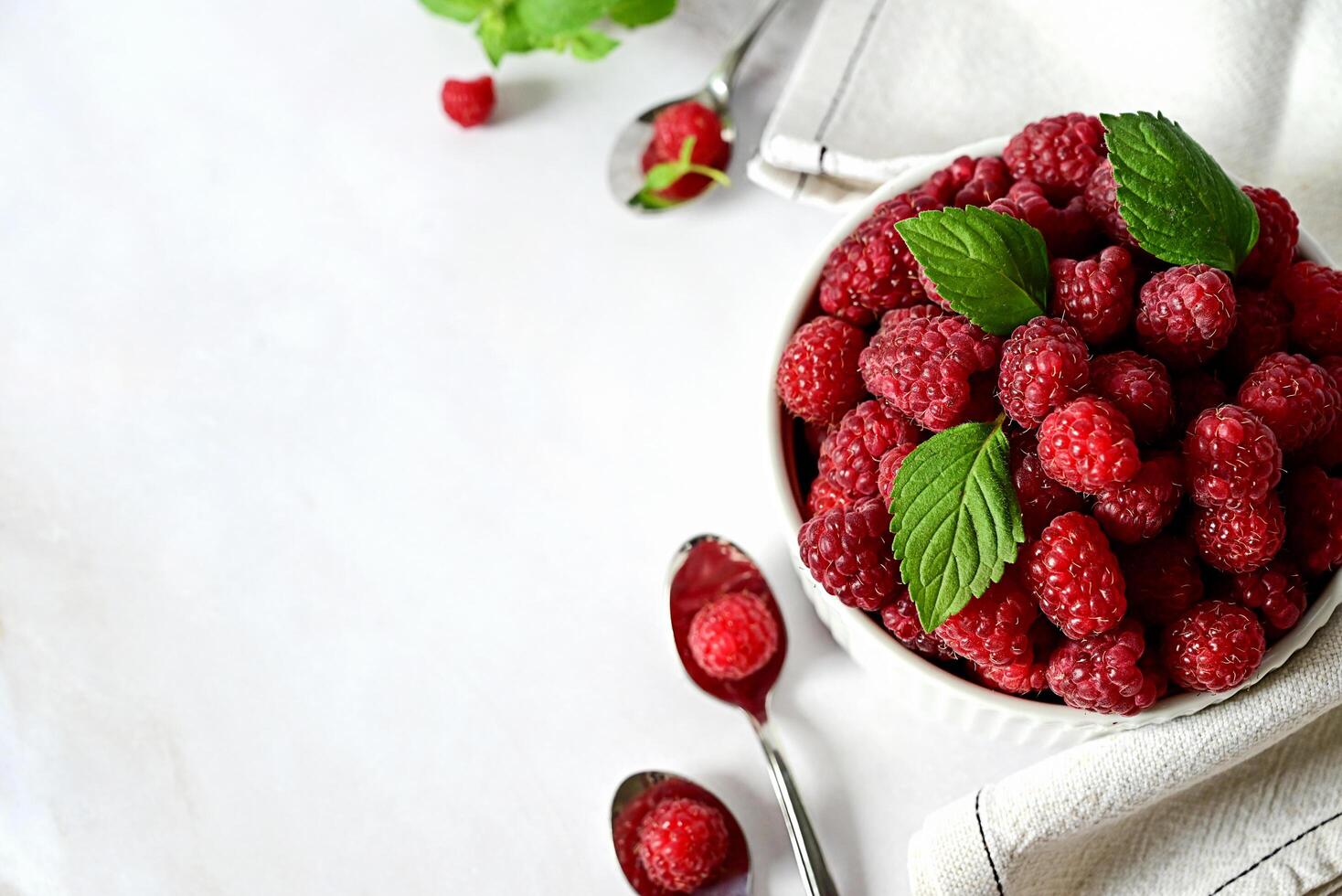 A Bowl of Red Raspberries on a Marble Background with Spoons photo