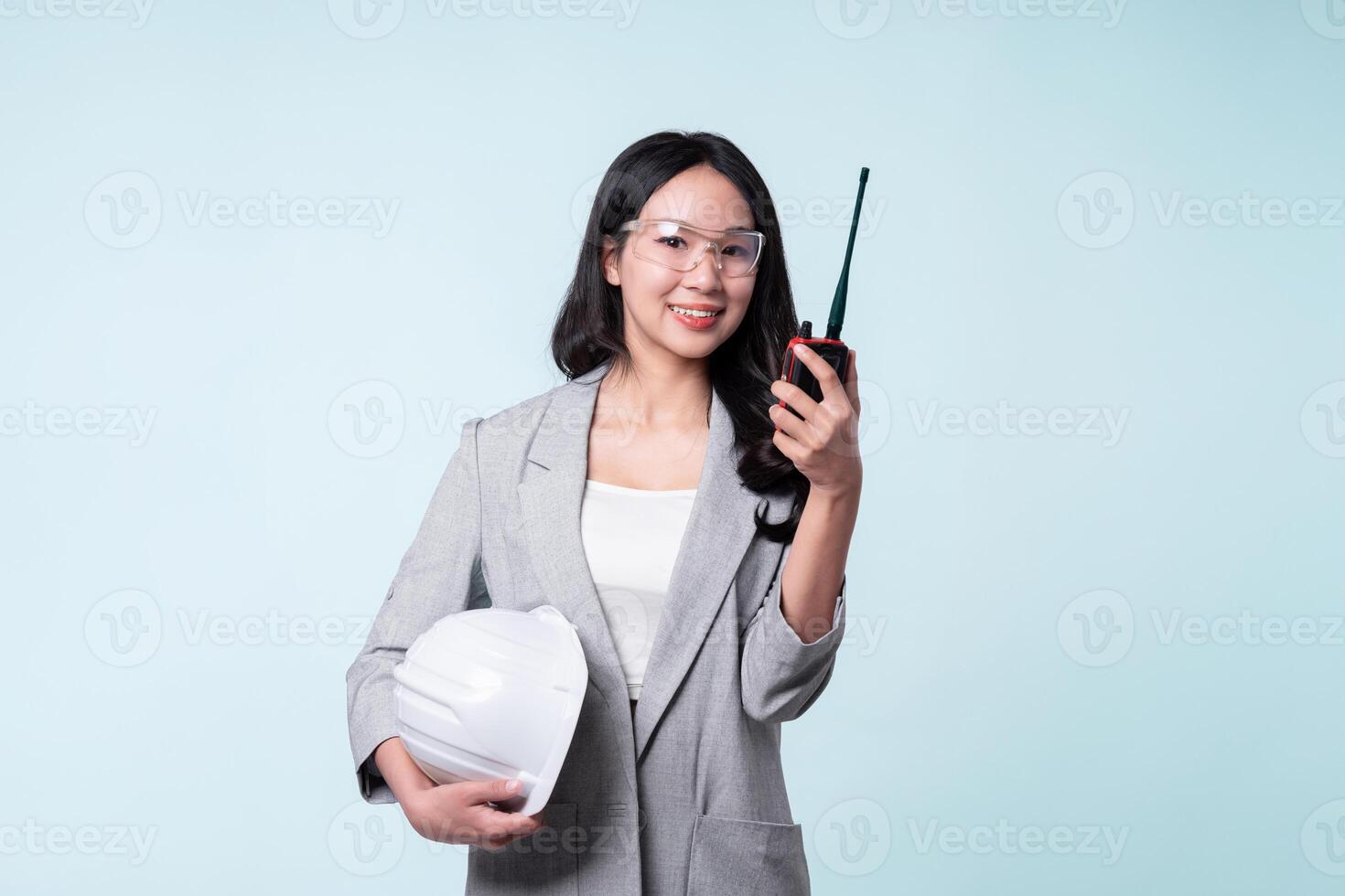 Confident woman engineer holding walkie talkie and white helmet isolated on light blue background. photo