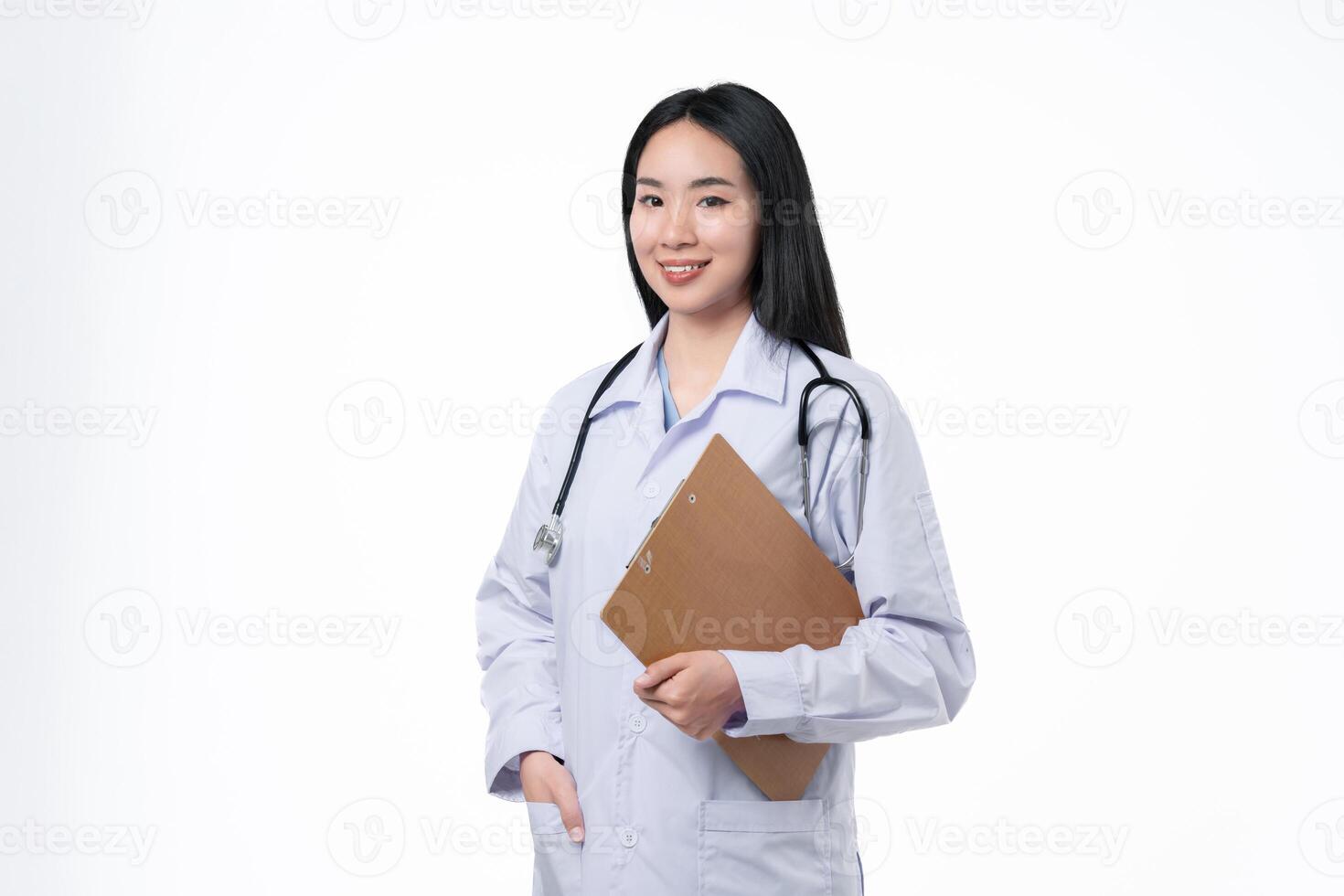 Young asian female doctor in uniform and stethoscope smiling and looking at camera while standing with clipboard in hands on white background. Healthcare and medical concept. photo