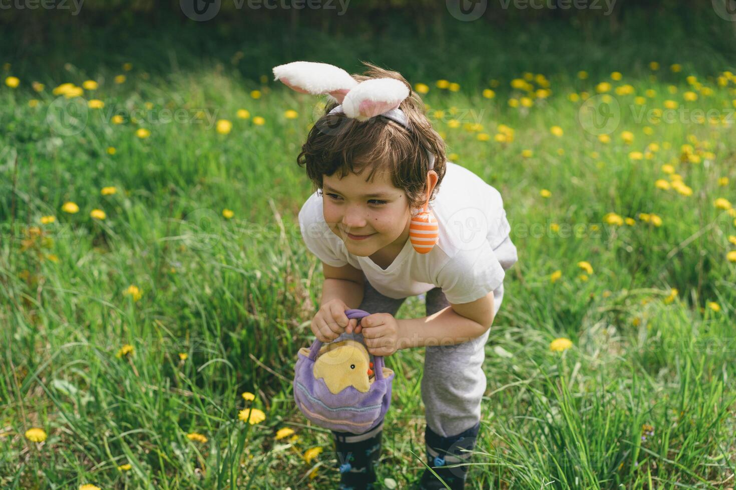 Boy with eggs basket and bunny ears on Easter egg hunt in sunny spring garden. photo
