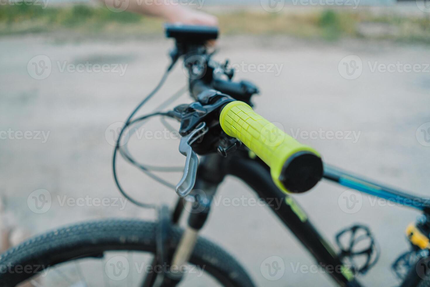 Closeup of a Black Mountain Bike Handlebars With Yellow Grips on a Dirt Road photo