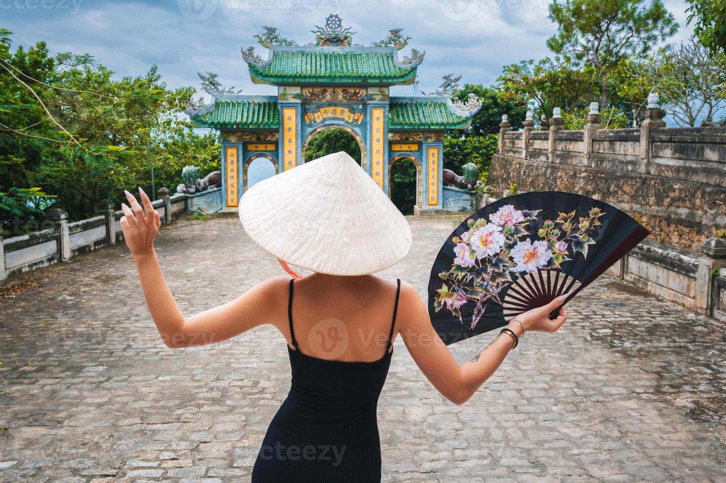Woman traveler visiting at Linh Ung Pagoda temple. Tourist with Vietnamese hat and with a fan traveling in Da Nang city. photo