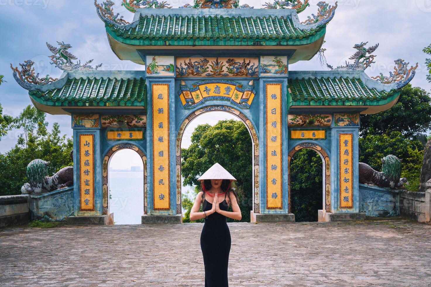 Woman traveler with Vietnamese hat and with a fan on the background at Linh Ung Pagoda temple traveling in Da Nang city. photo