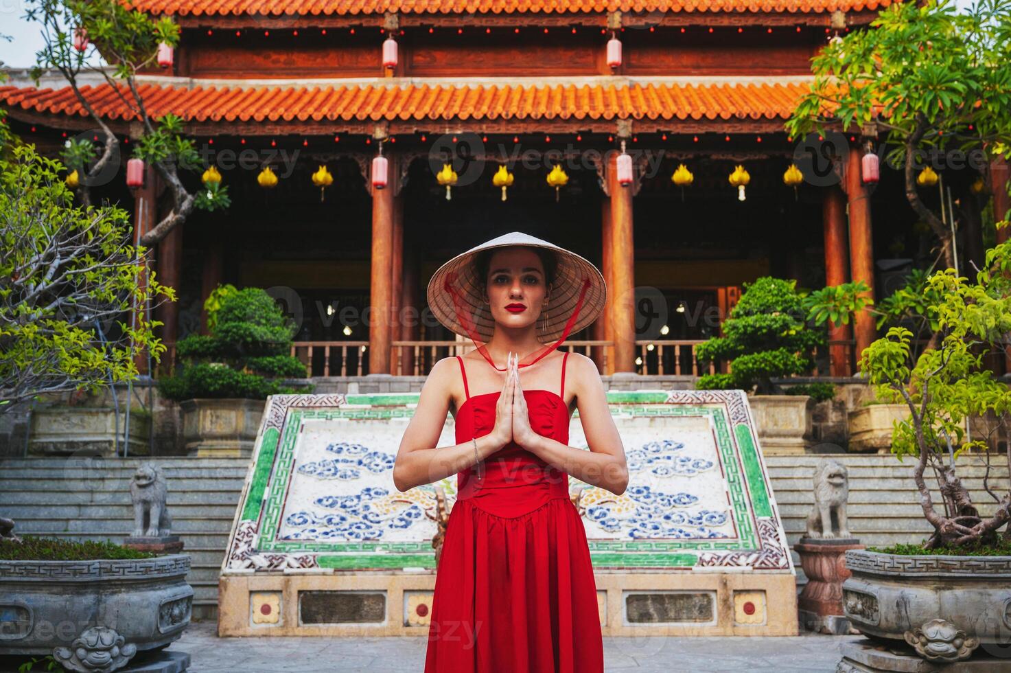 Portrait of a female tourist with her arms crossed over her chest in a traditional Vietnamese conical headdress against the backdrop of a pagoda in Nha Trang photo