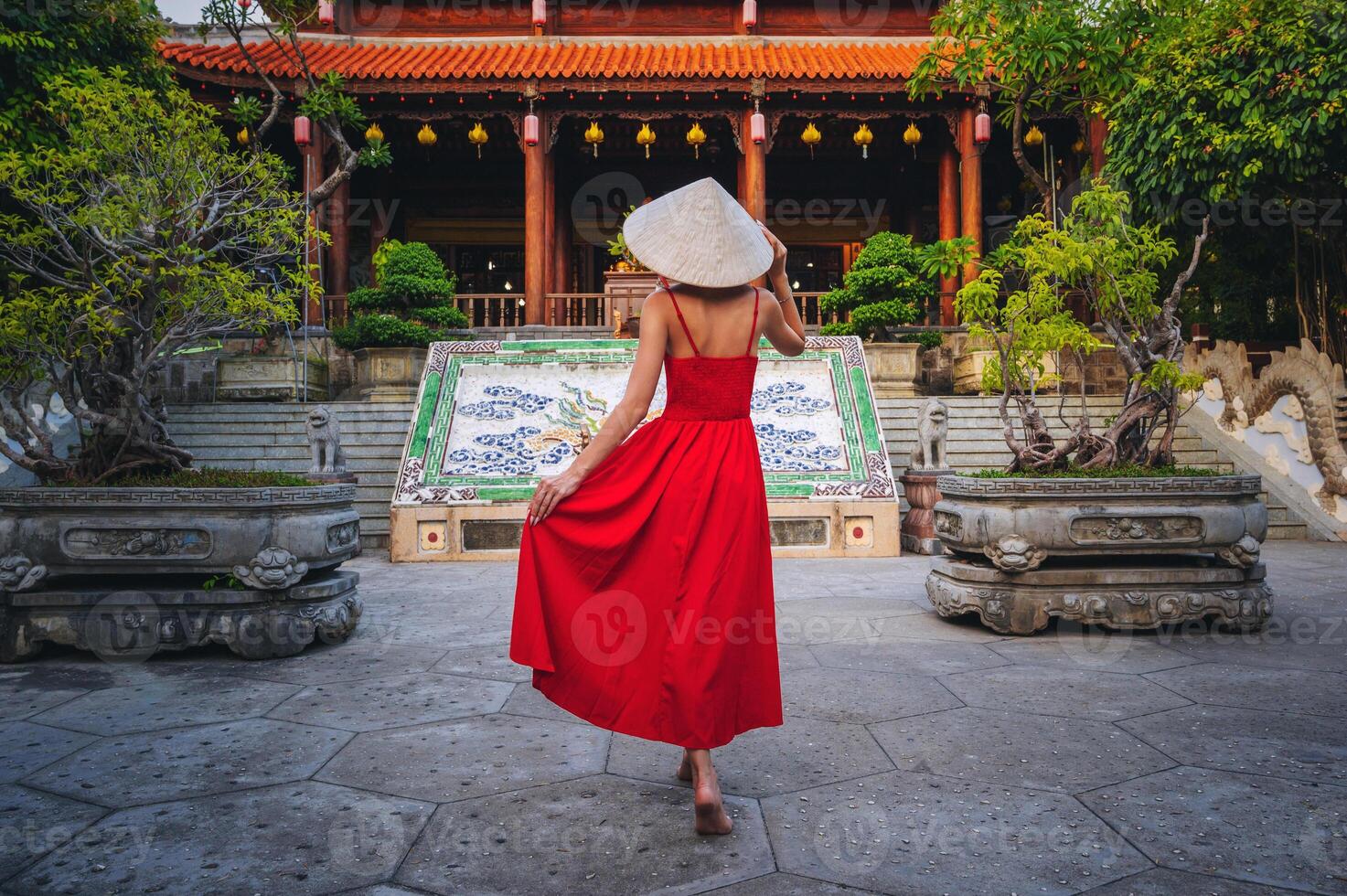 Tourists in a red dress and a traditional Vietnamese headdress in the shape of a cone against the backdrop of a pagoda in Nha Trang photo