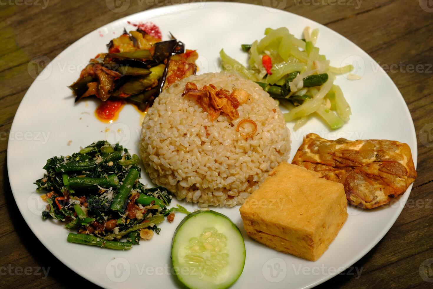 Nasi Campur Vegetarian is is brown rice with sauted green vegetables, sambal, sliced cucumber and tomato slices, fried tofu, and fried tempeh. Suitable for vegetarians. Indonesian food. Nasi Rames. photo