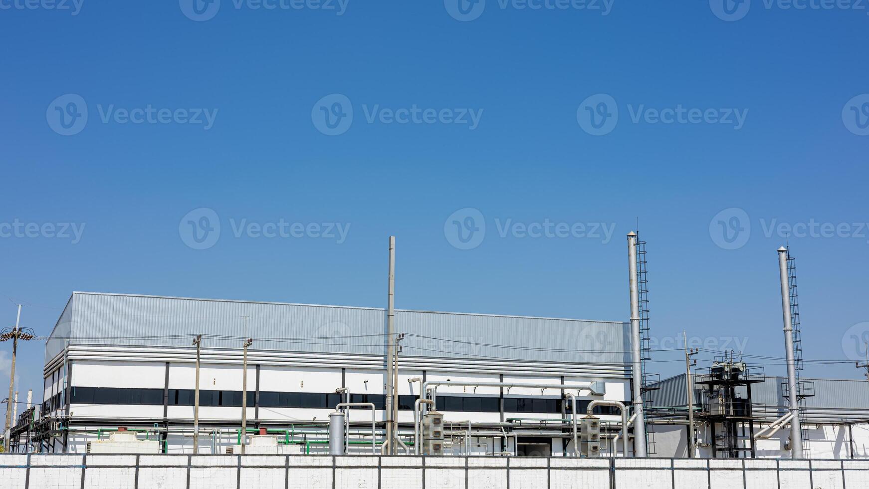 Back of industrial factory building with ventilation ducts and pipes, chimneys with electric poles and wires. The building has aluminum walls with blue sky background. Horizontal side view. photo