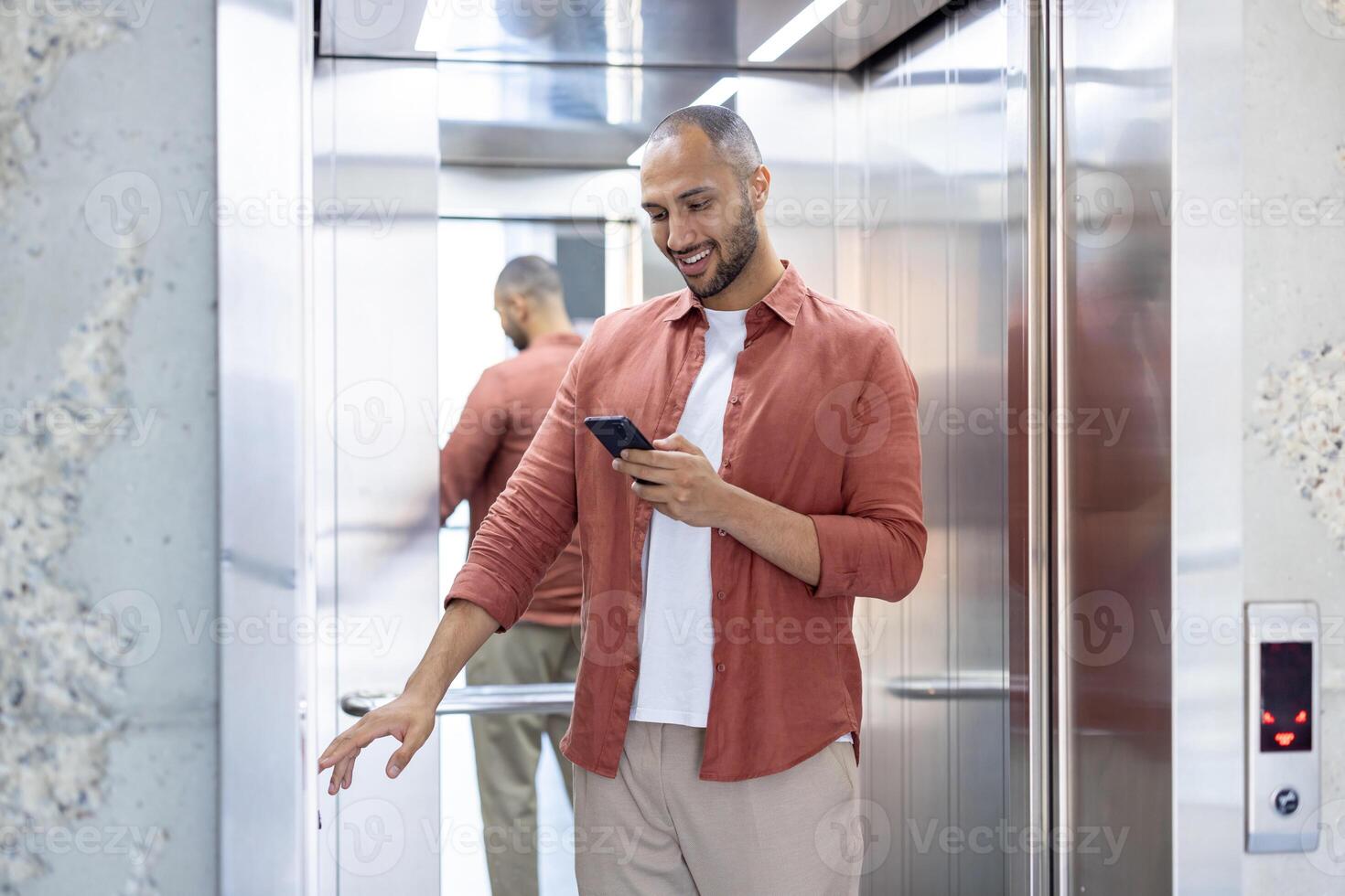 A young man wearing casual attire checks his smartphone while entering an elevator. The scene emphasizes modern technology usage in everyday activities. photo