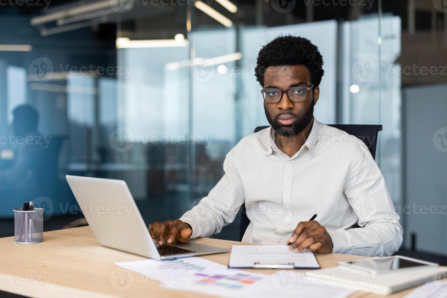 Portrait of successful serious financier accountant at workplace, man looking focused at camera. Businessman doing paperwork inside office, working with contracts and reports, documents. photo