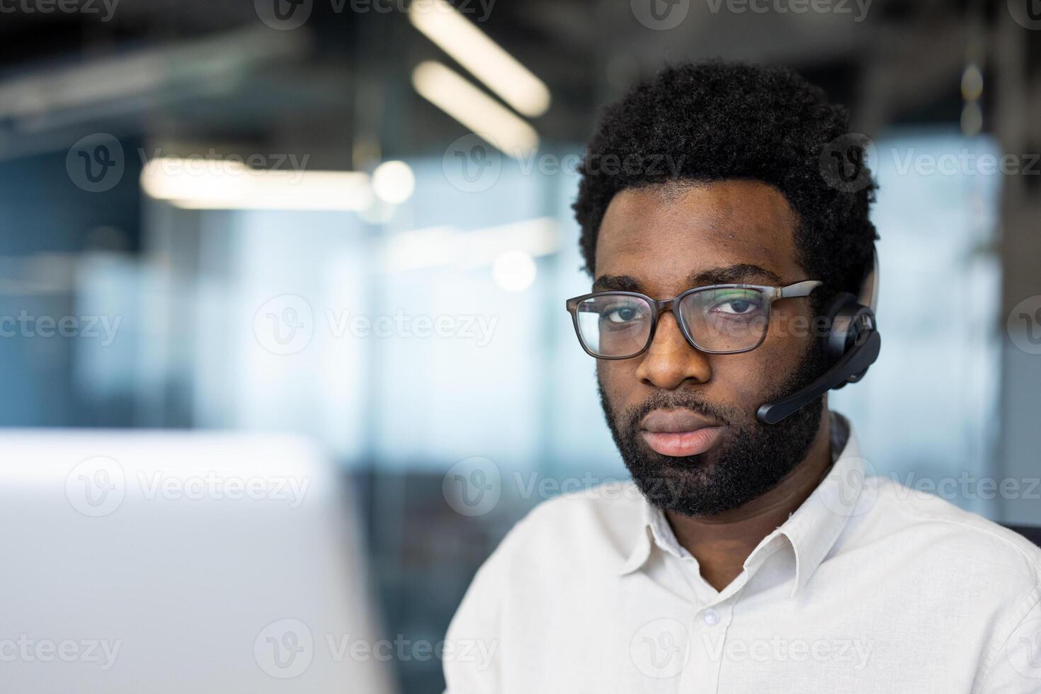 Portrait of serious thinking man with headset, office worker looking at camera, working inside office with laptop close-up. photo