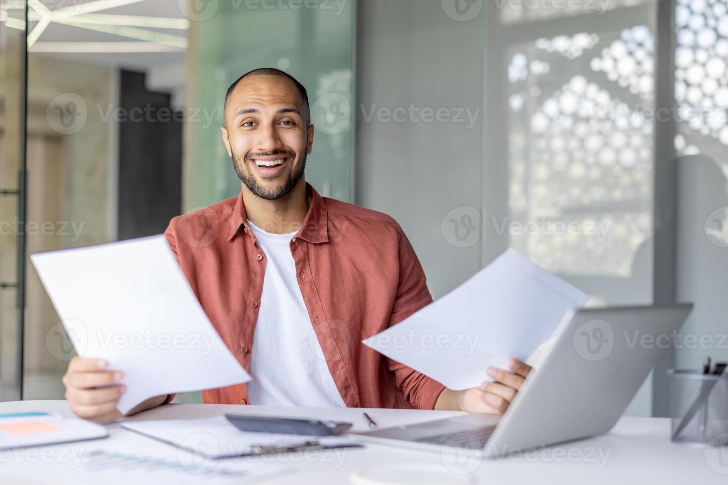 Portrait joyful successful financier, man with documents and financial reports in his hands smiles and looks at the camera. Businessman works inside the office with bills, satisfied with the results. photo