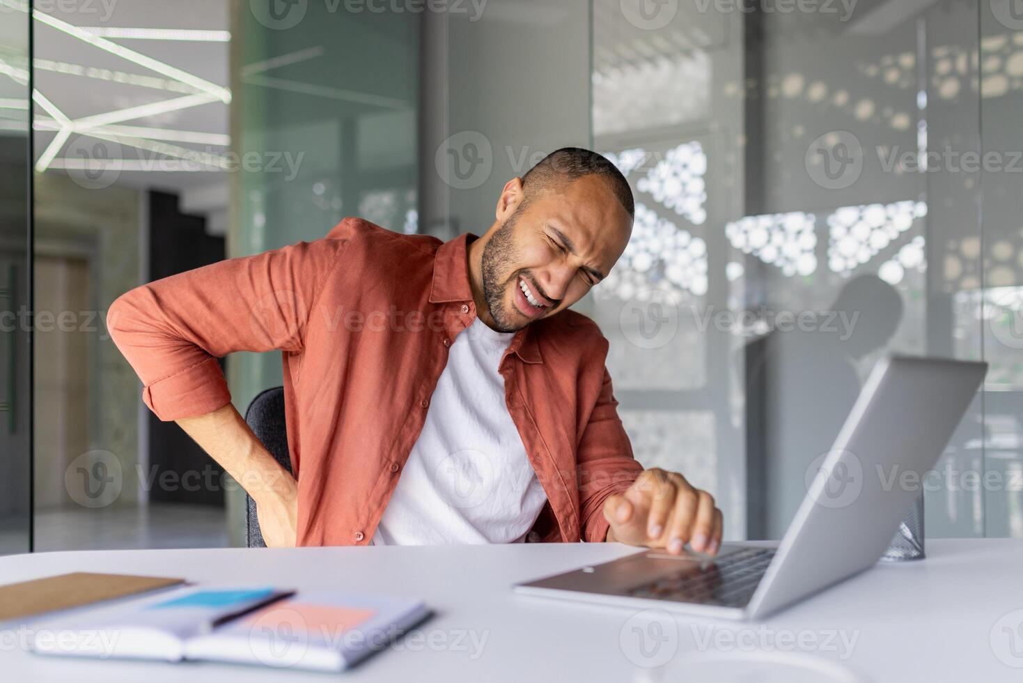 Man experiencing back pain while working at office desk with laptop. Concept of discomfort, posture issues, and need for ergonomic workspace during work. Focus on health. photo