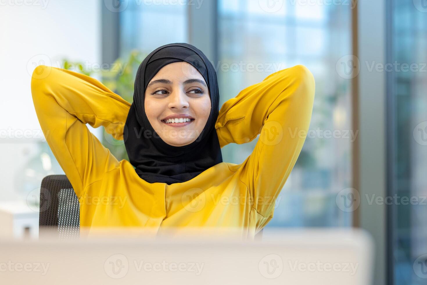 Successful woman completed work, businesswoman in hijab well done put her hands behind her head smiling and looking out the window, satisfied with the results of the achievement inside the office. photo