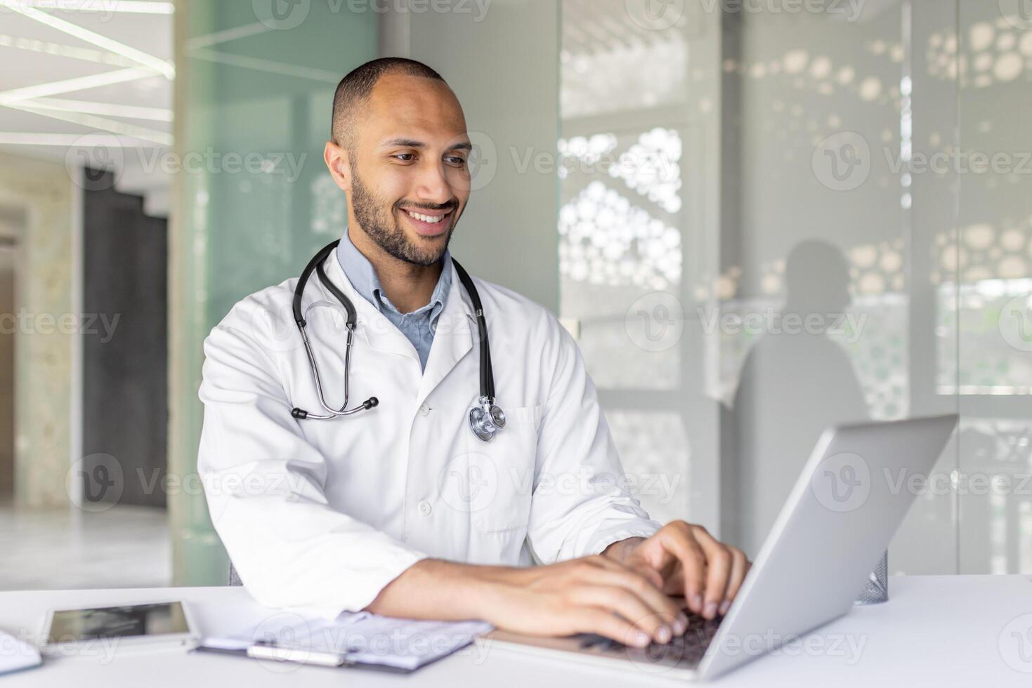 A smiling doctor is using a laptop in a modern office setting, showcasing productivity and professionalism. The image captures a sense of technology integration in the healthcare field. photo