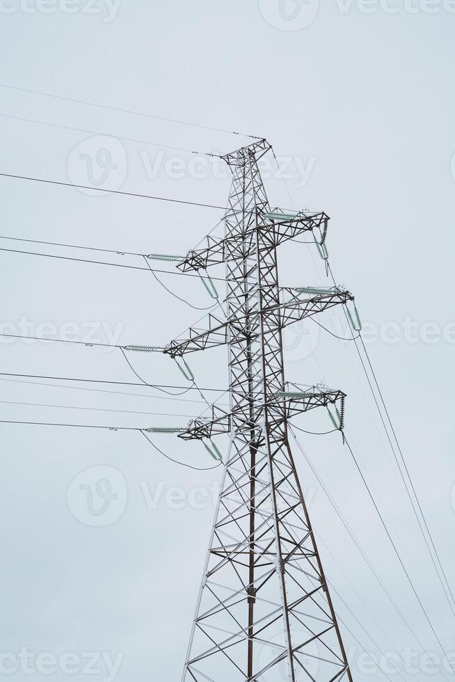 A tall High Voltage Power Line Tower rises against a slightly overcast sky with clouds photo