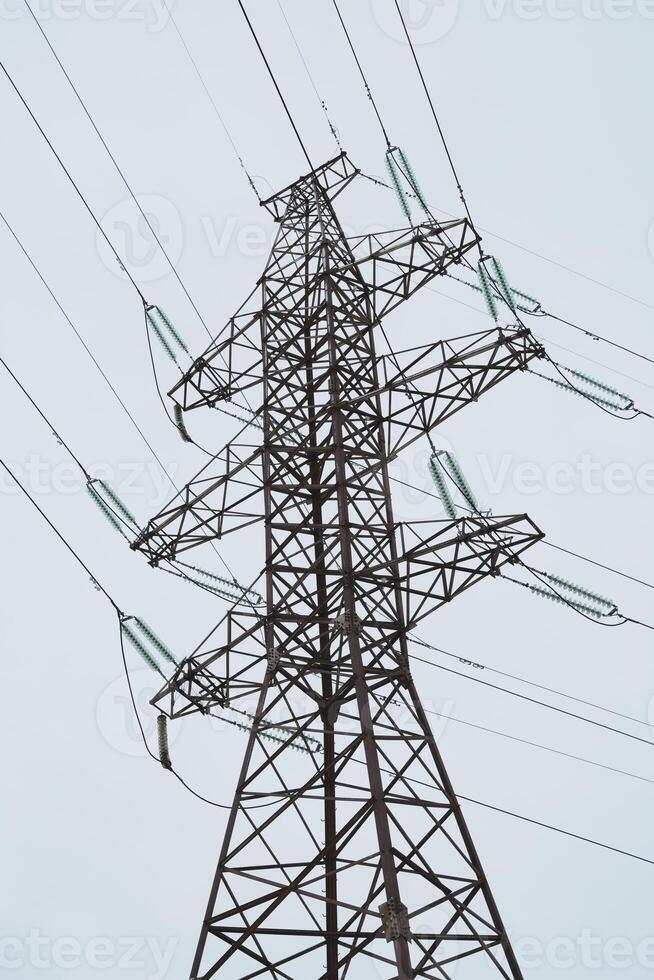 A tall High Voltage Power Transmission Tower stands prominently against a cloudy overcast sky photo