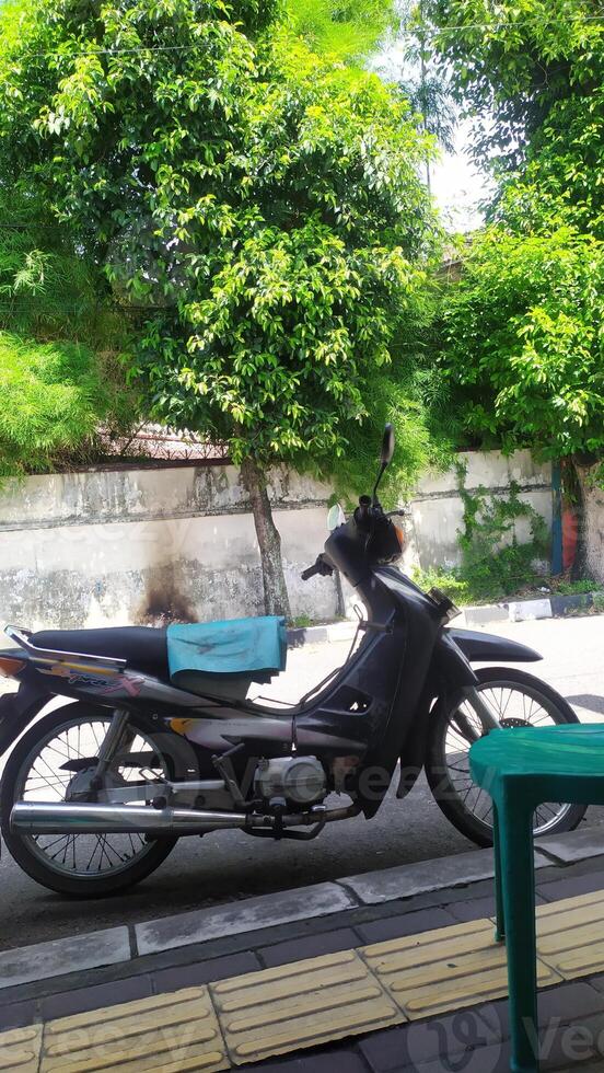 a motor bike parked on the sidewalk, shady trees on the side of the road photo