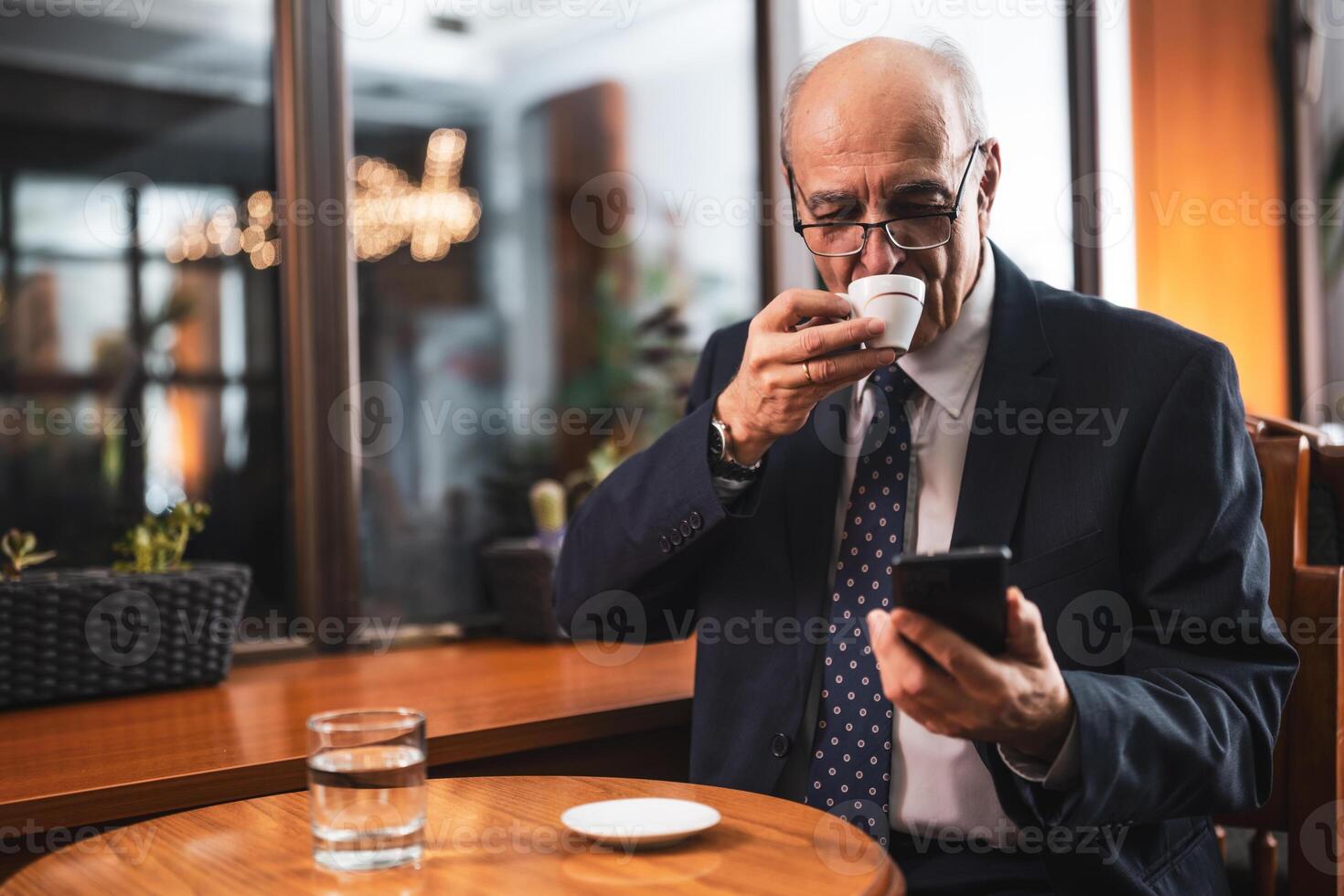 Senior businessman enjoying drinking coffee and using mobile phone while sitting in the cozy cafeteria. photo