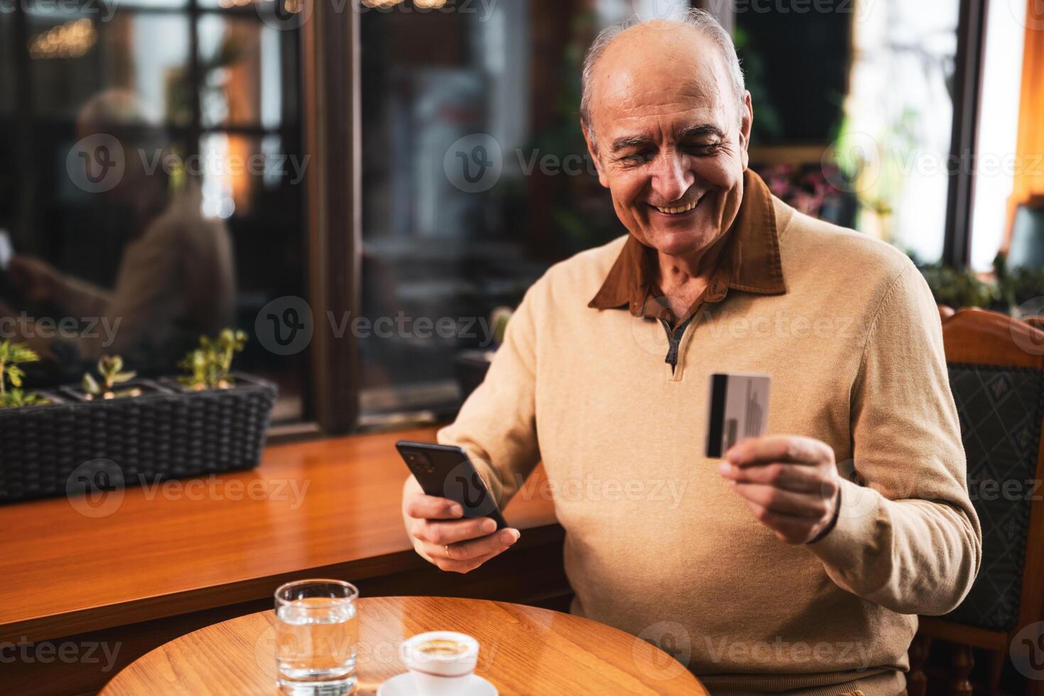 Senior man using smart phone and credit card while drinking coffee in the city cafe. photo