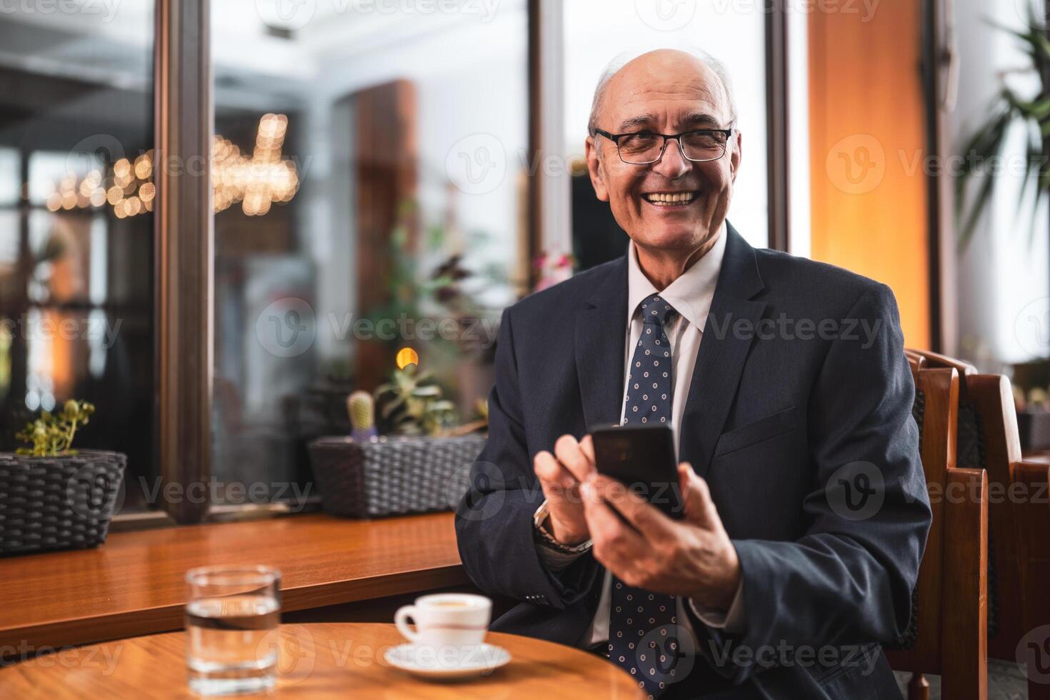 Older businessman sitting in cafe and checking messages on his smart phone. photo