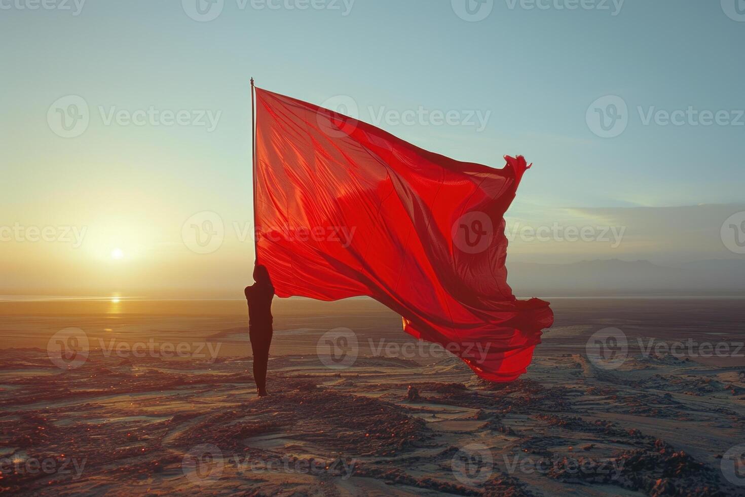 Person standing on a rocky beach holding a giant red flag at sunset photo