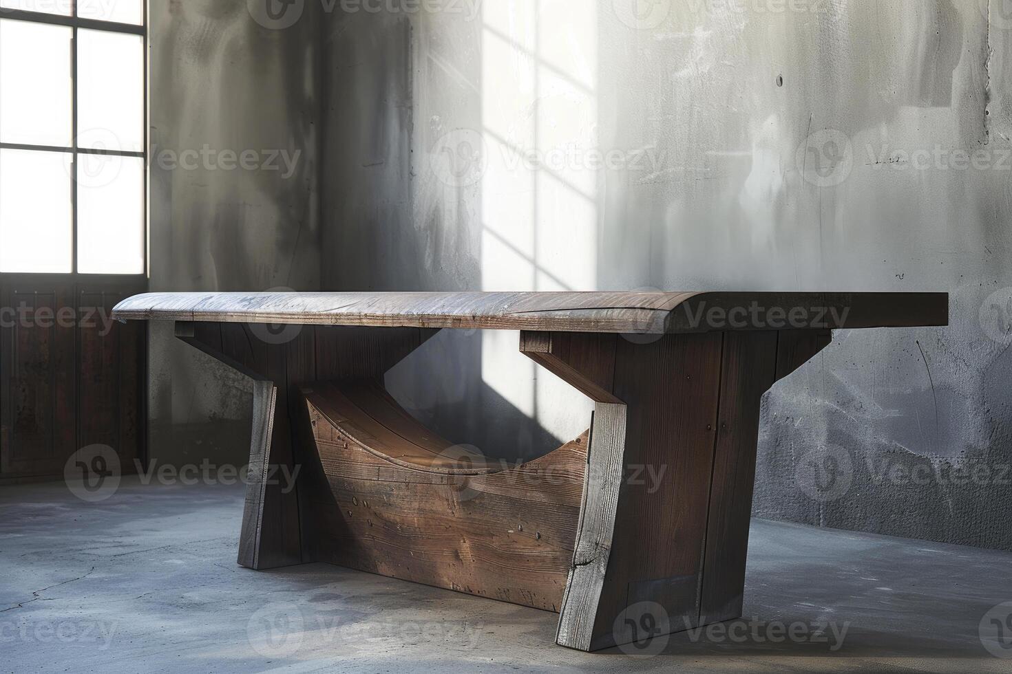 Large wooden table standing in a sunlit room with a concrete floor photo
