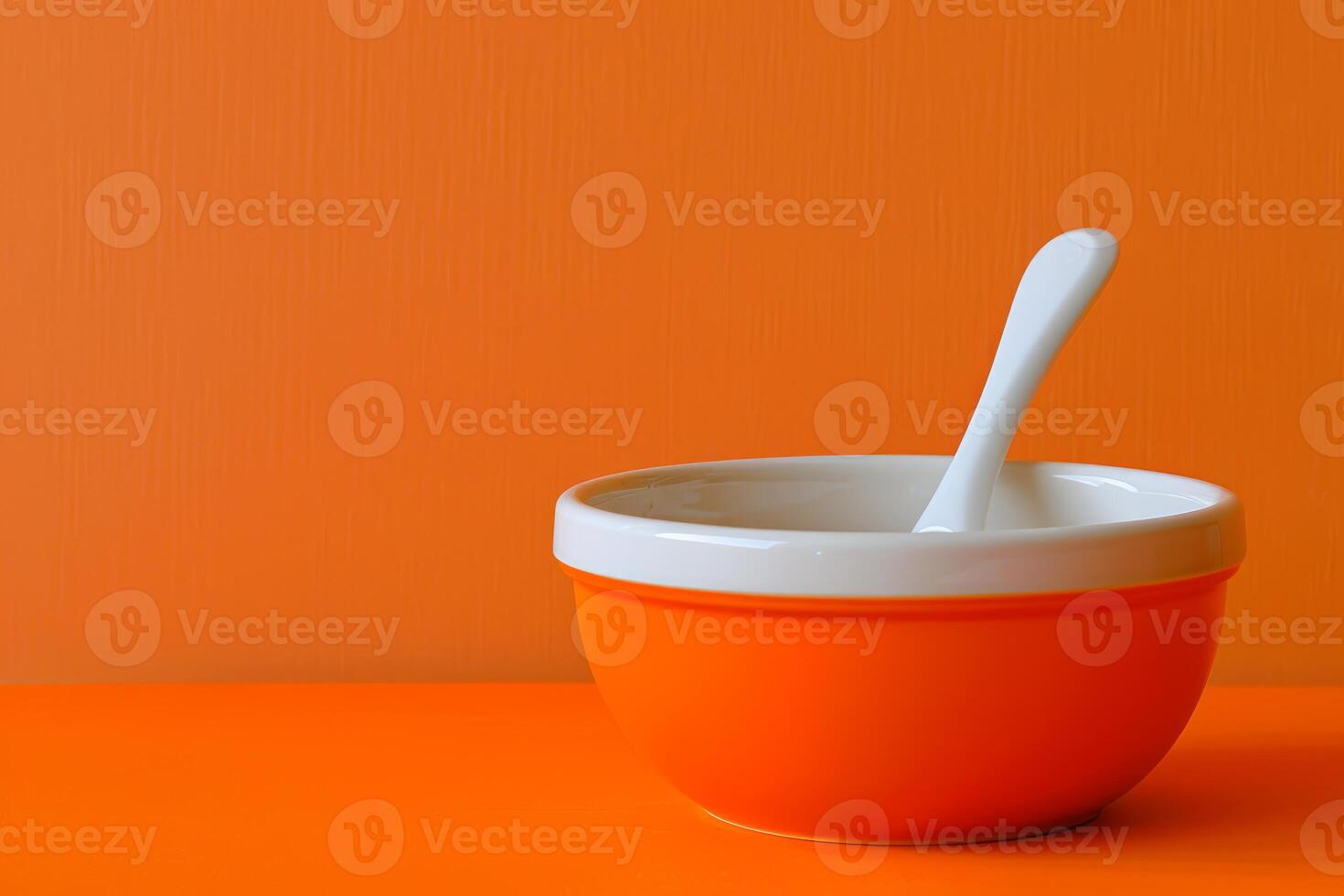 Orange bowl with white spoon on orange background photo