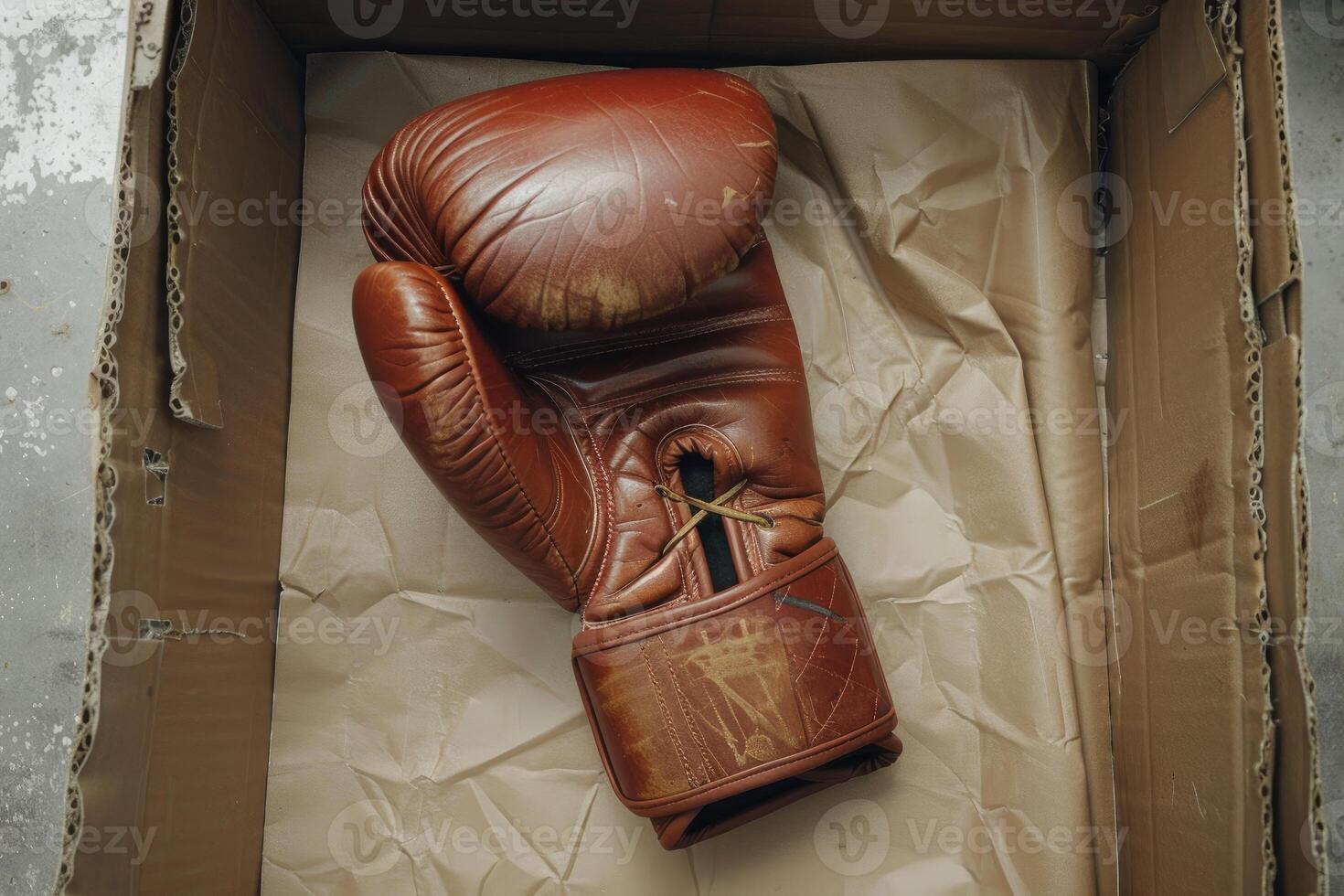 Old leather boxing glove resting in cardboard box on crumpled paper photo