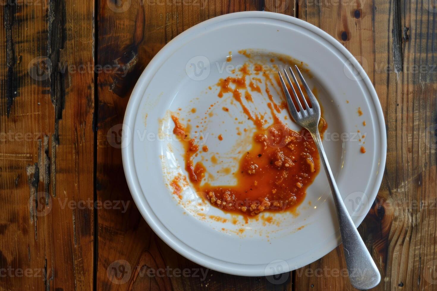 Empty plate with tomato sauce leftovers and fork on wooden table photo
