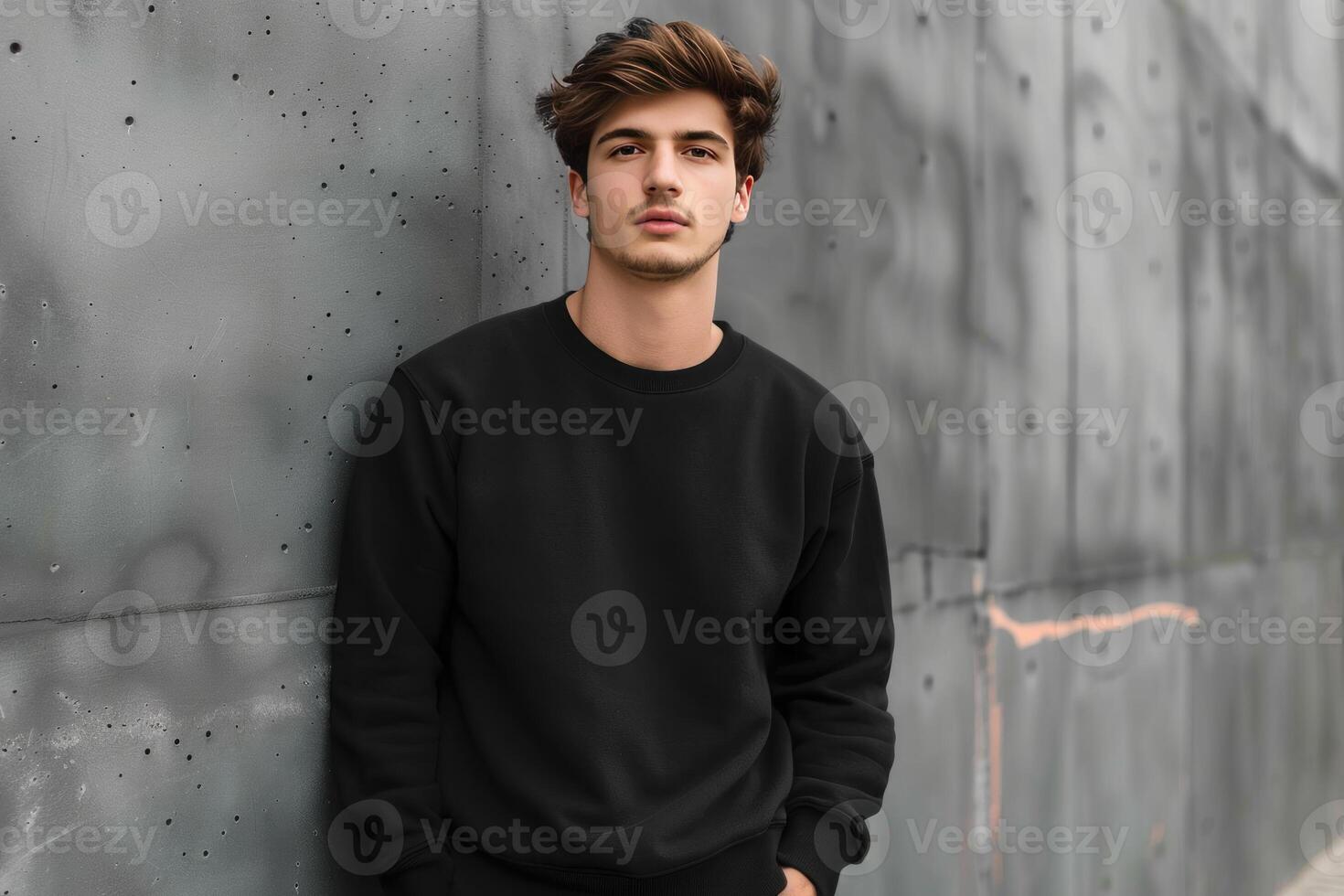 Young man leaning against gray wall wearing black sweatshirt photo