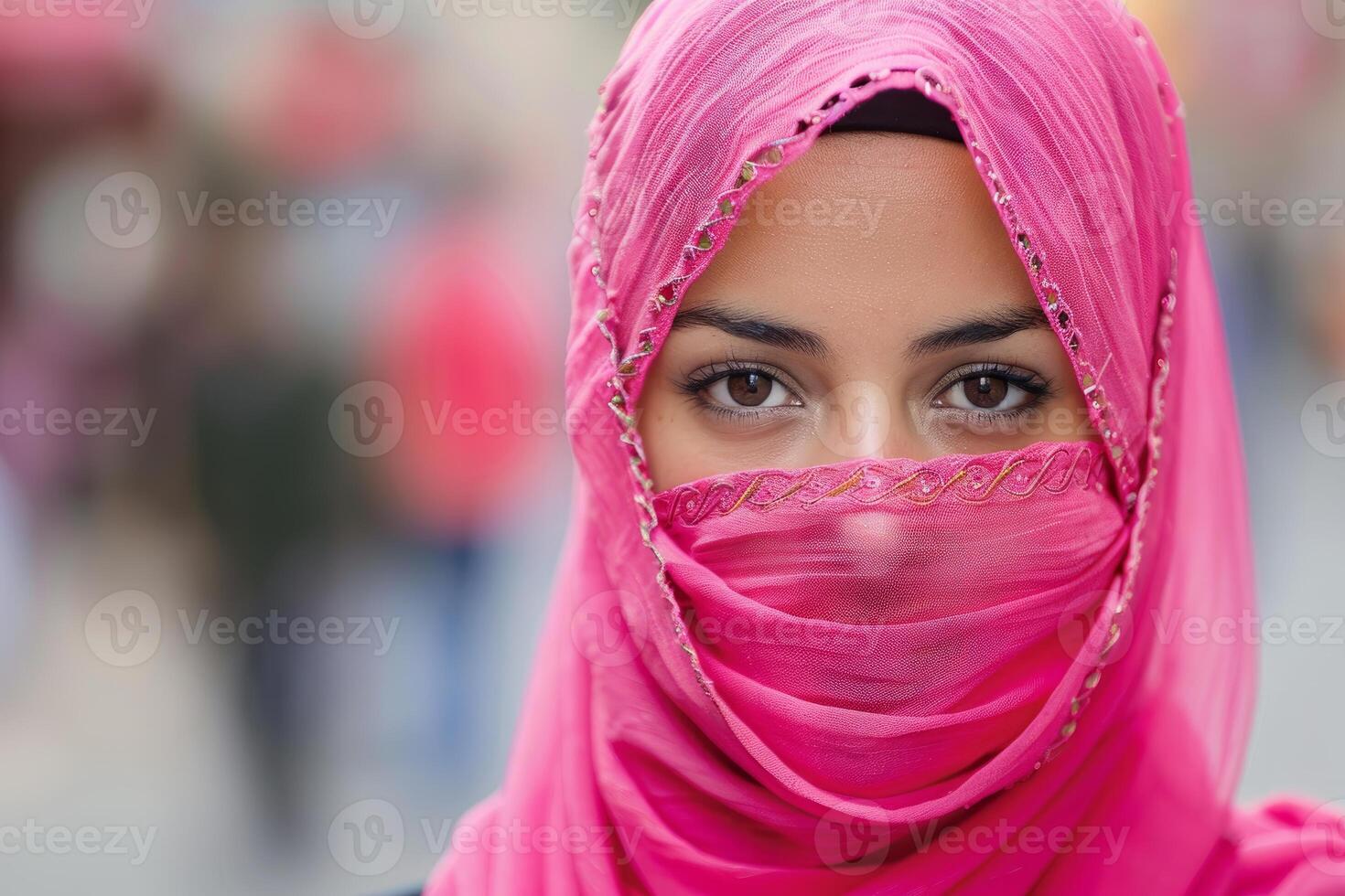 Muslim woman wearing a pink niqab and hijab in a blurred urban setting photo
