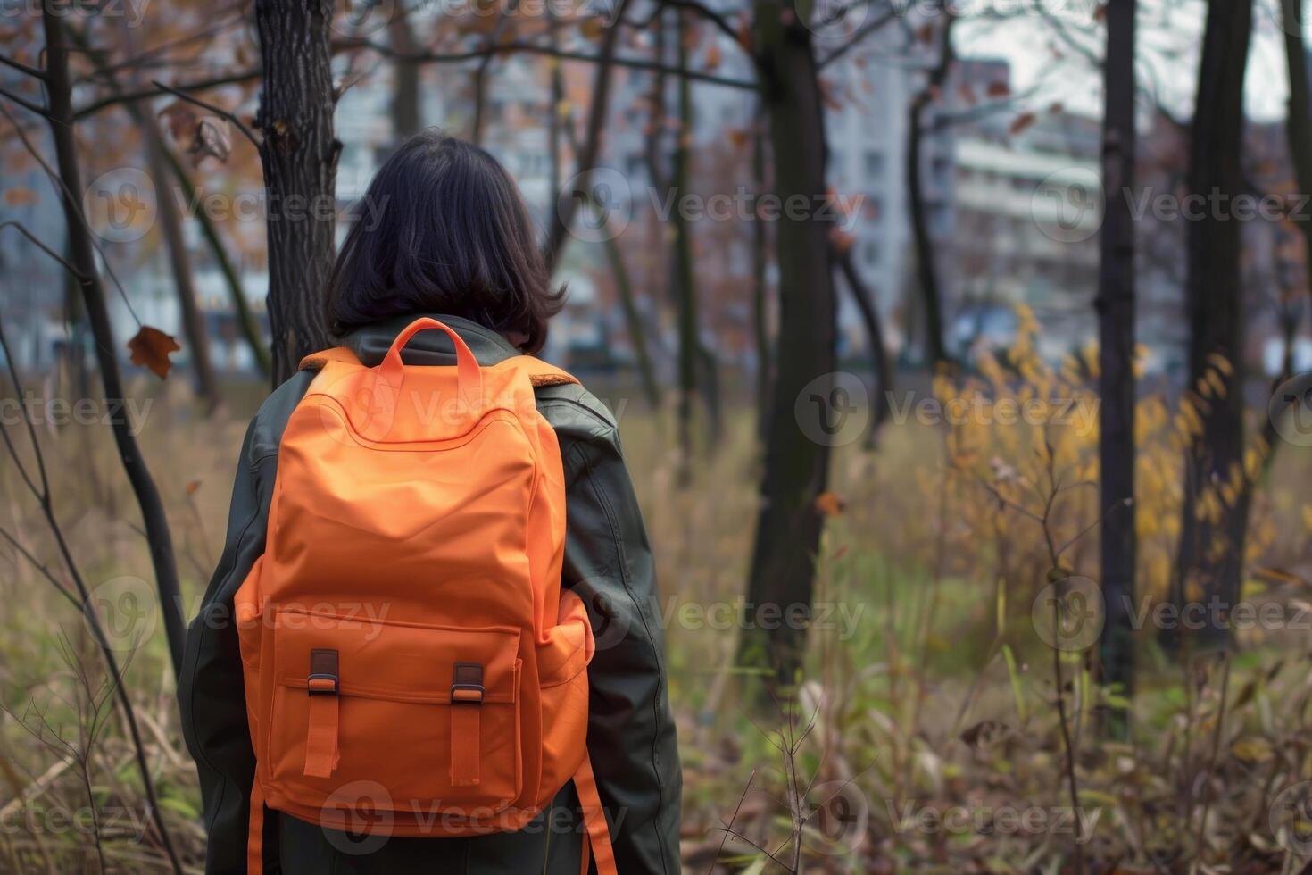 Student walking away in autumn forest near city with orange backpack photo