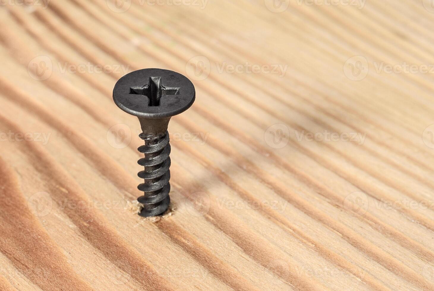 Black screw screwed into wood. Construction and repair photo