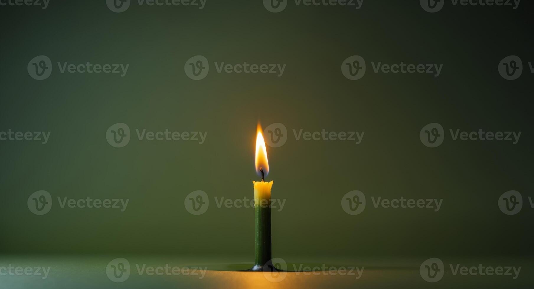 A single yellow candle flame illuminating a dark green background with space for text. photo