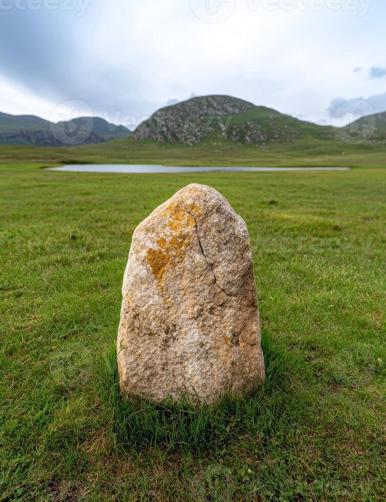 Single standing stone in a grassy field with mountains in the background photo