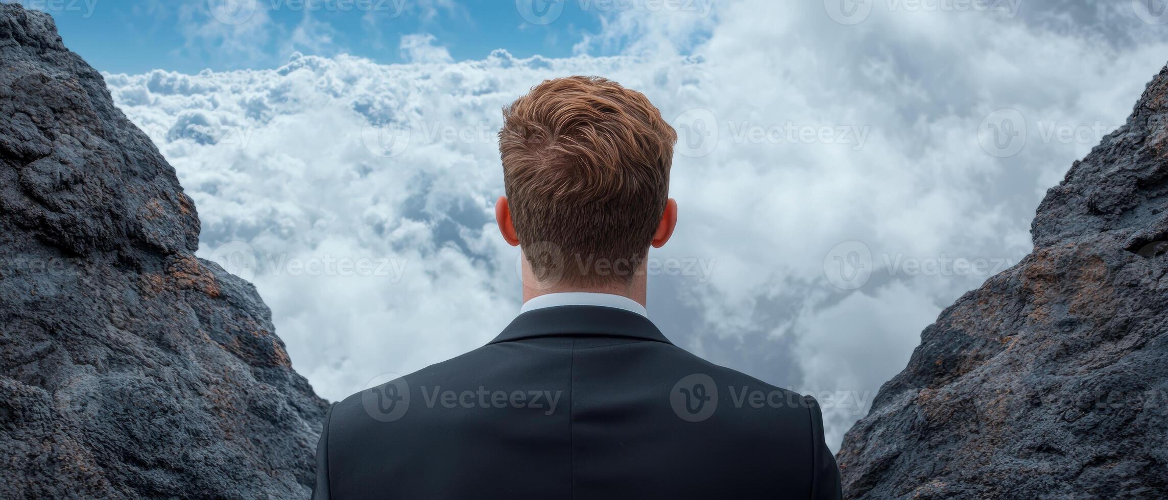 Businessman standing at the edge of a cliff looking out at the clouds photo