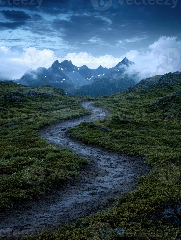 A winding path leads through a lush green landscape towards majestic mountains under a dramatic sky photo