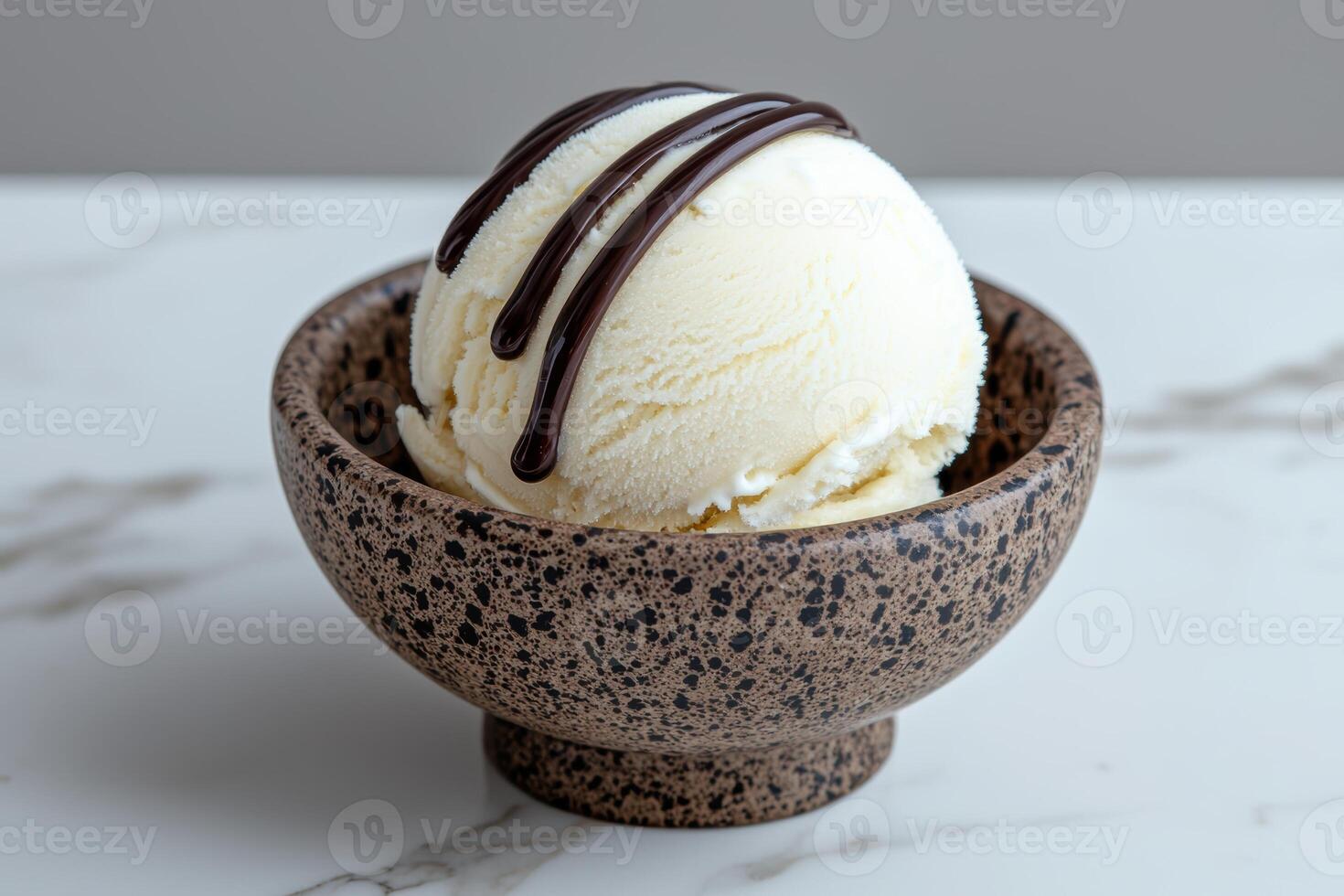 A scoop of vanilla ice cream with chocolate syrup in a small bowl photo