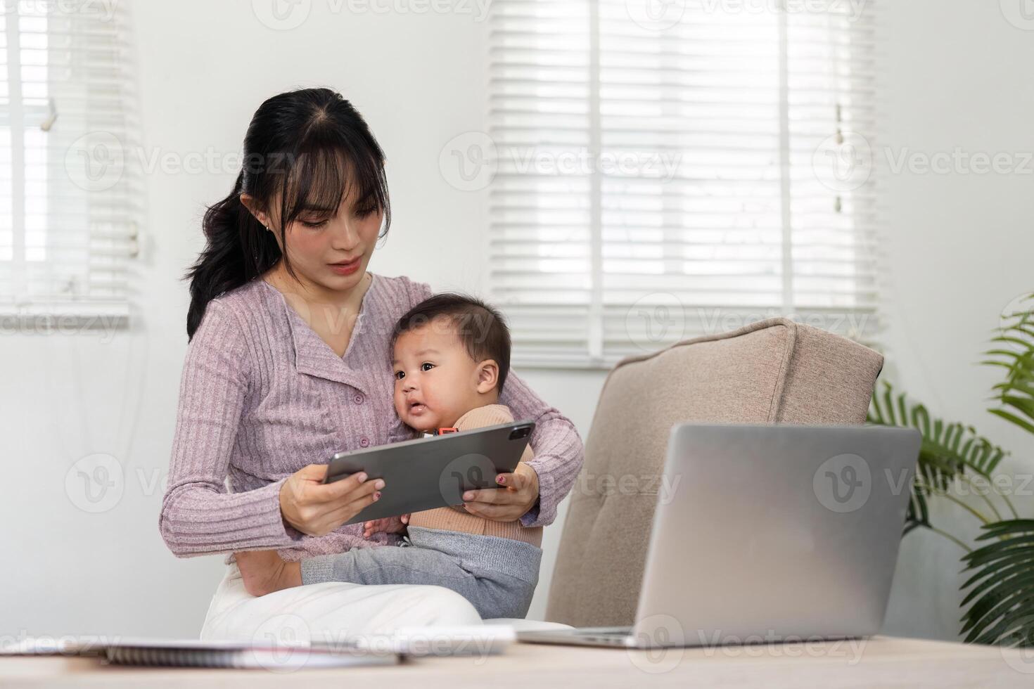 Interactive mother engaging with her baby on a tablet while managing tasks in a home office photo