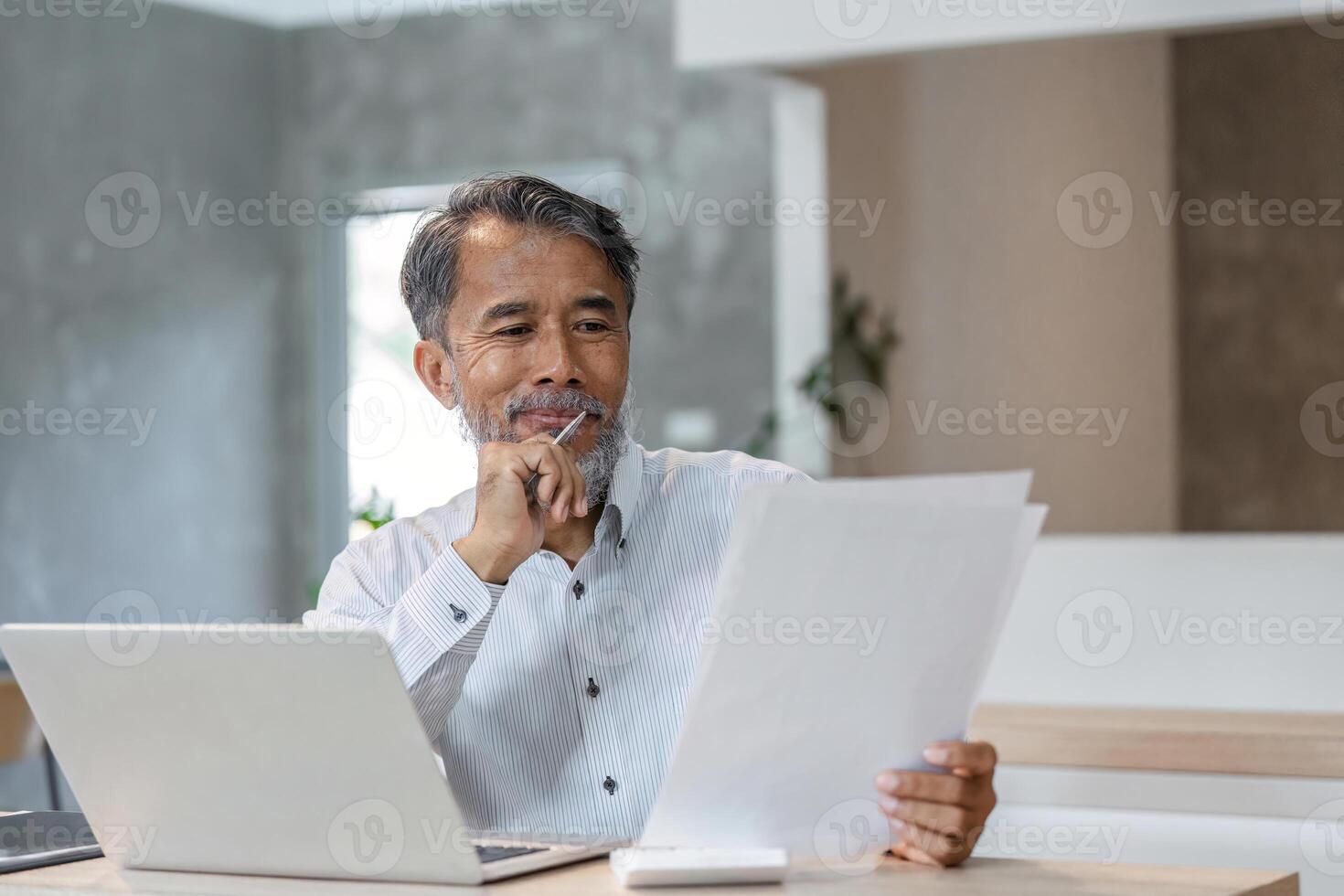 Thoughtful male businessman analyzing documents at his desk with laptop in contemporary workspace photo