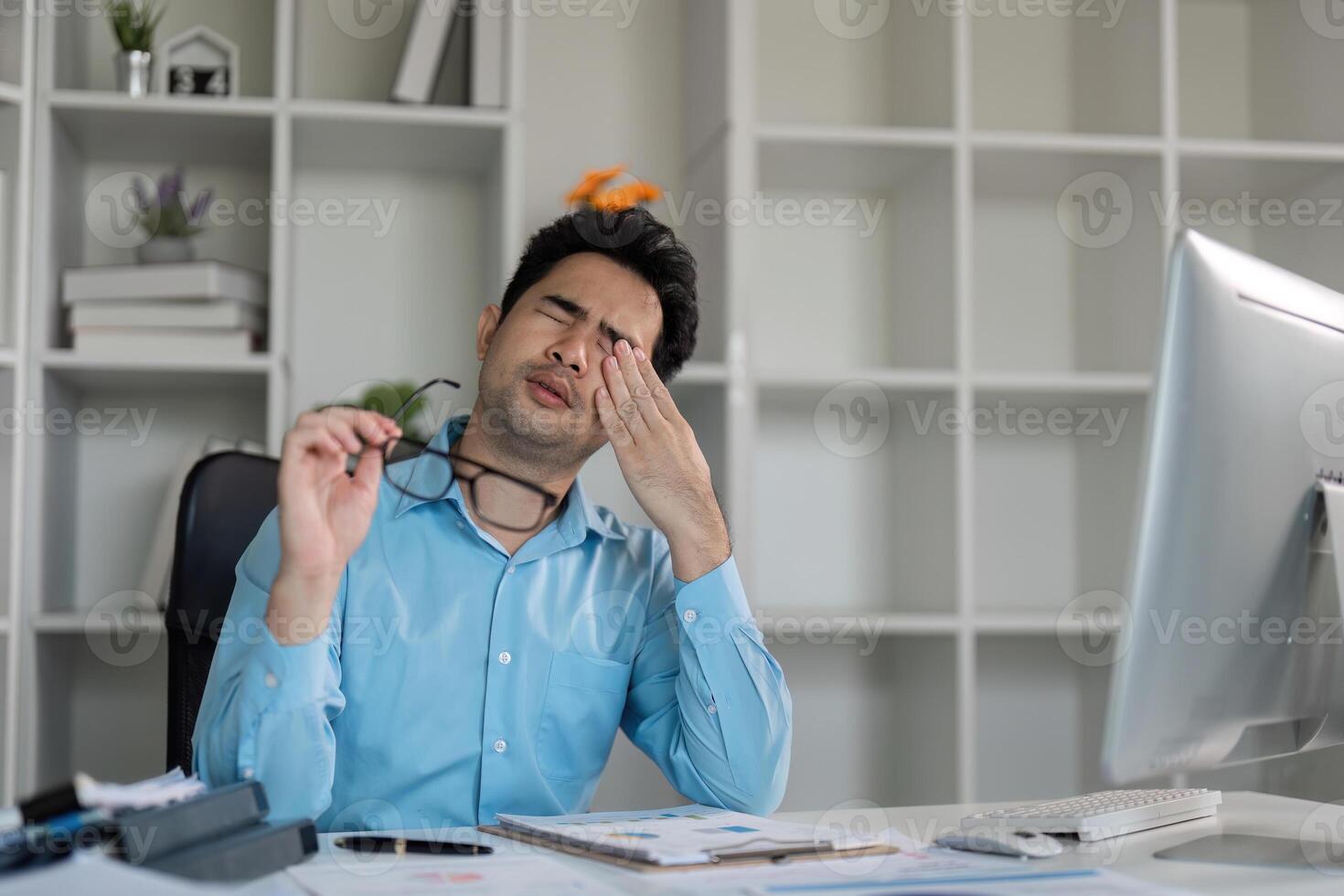 Stressed Young Businessman at Office Desk Struggling with Workload and Deadlines in Modern Corporate Environment photo