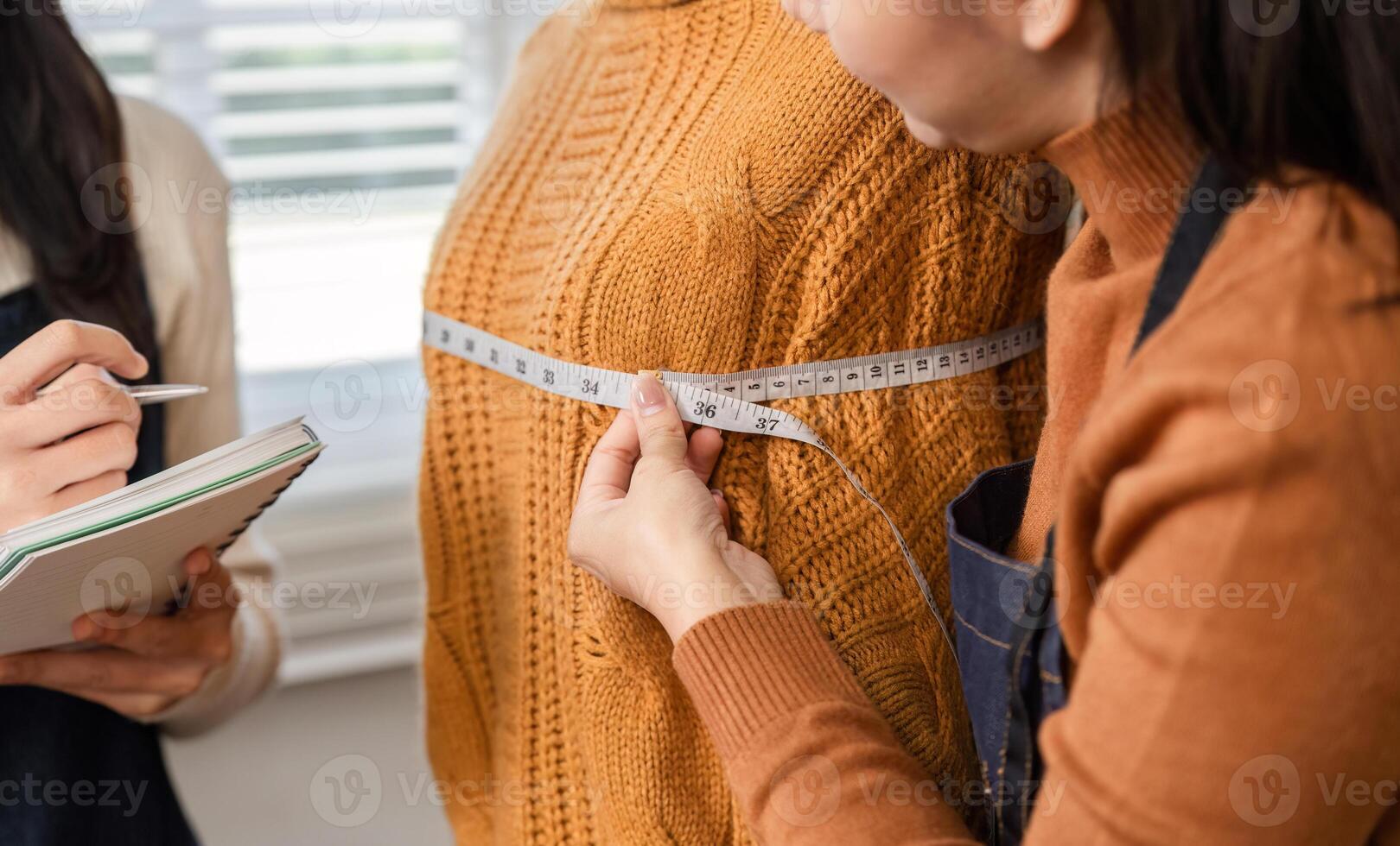 Fashion designer taking measurements for custom garment fitting with model in cozy knit sweater photo