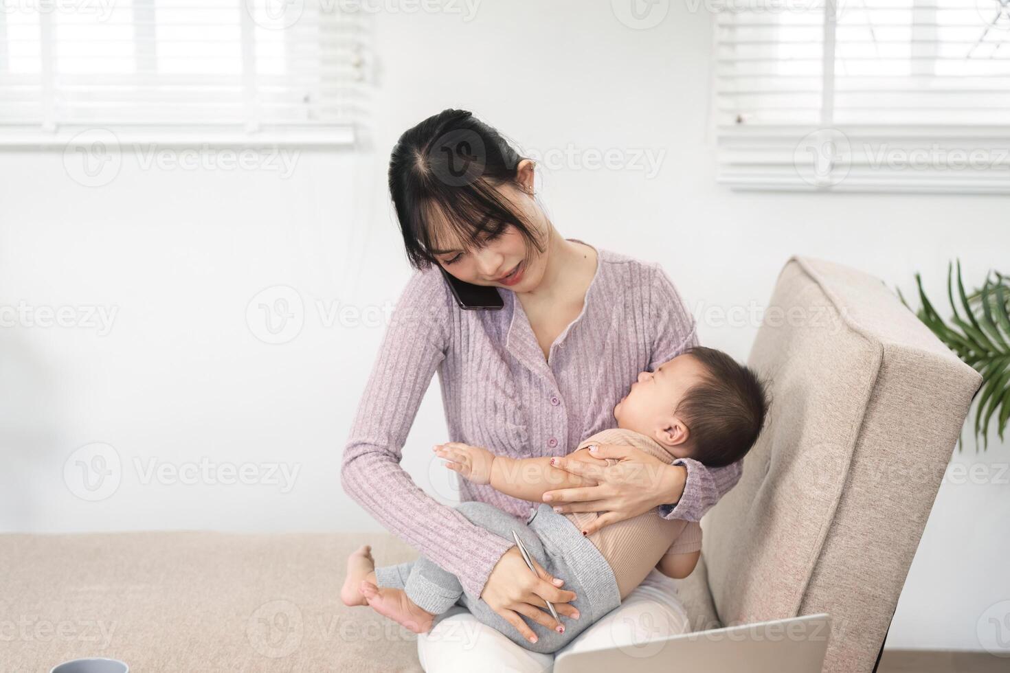 Single mom balancing work and parenting while discussing tasks on the phone with her baby in her lap photo
