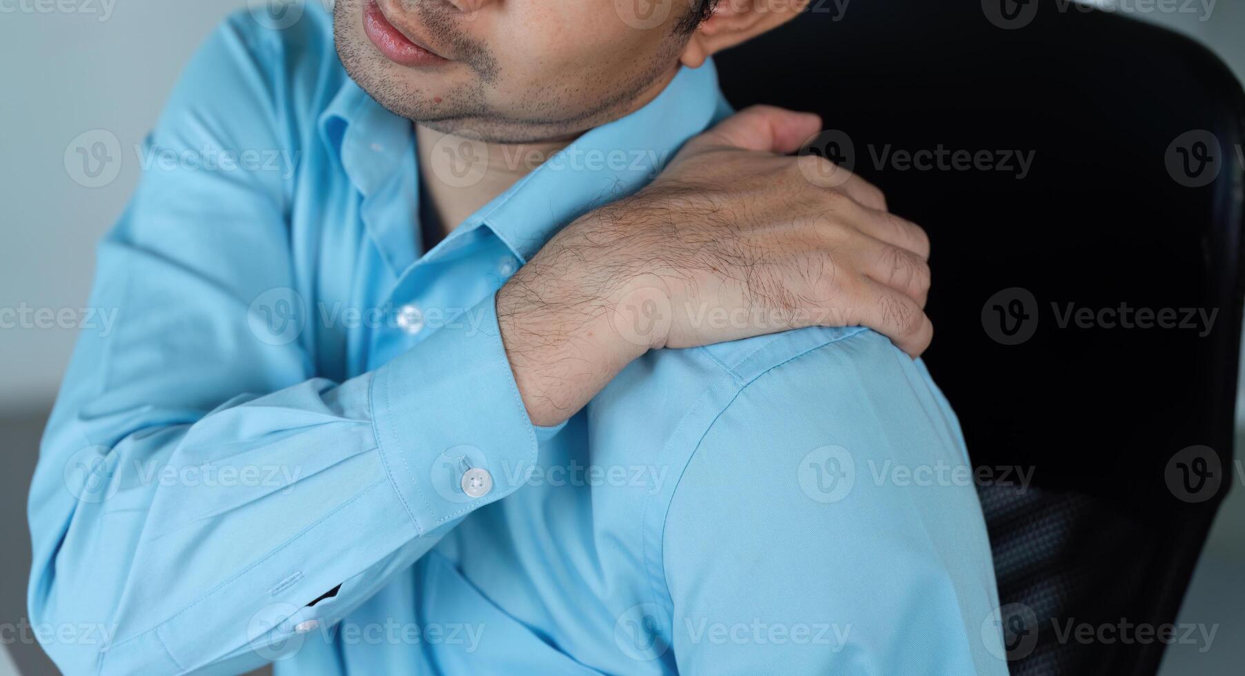 Young Businessman in Office Experiencing Aches and Pains While Working at Desk in Modern Corporate Environment photo