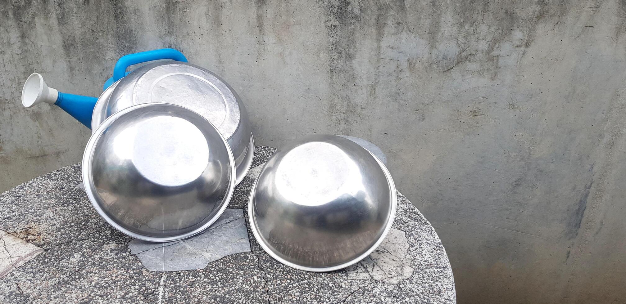 Group of stainless steel bowl putting and blue plastic watering can on stone table with gray concrete wall background and right copy space. Group of object concept. photo