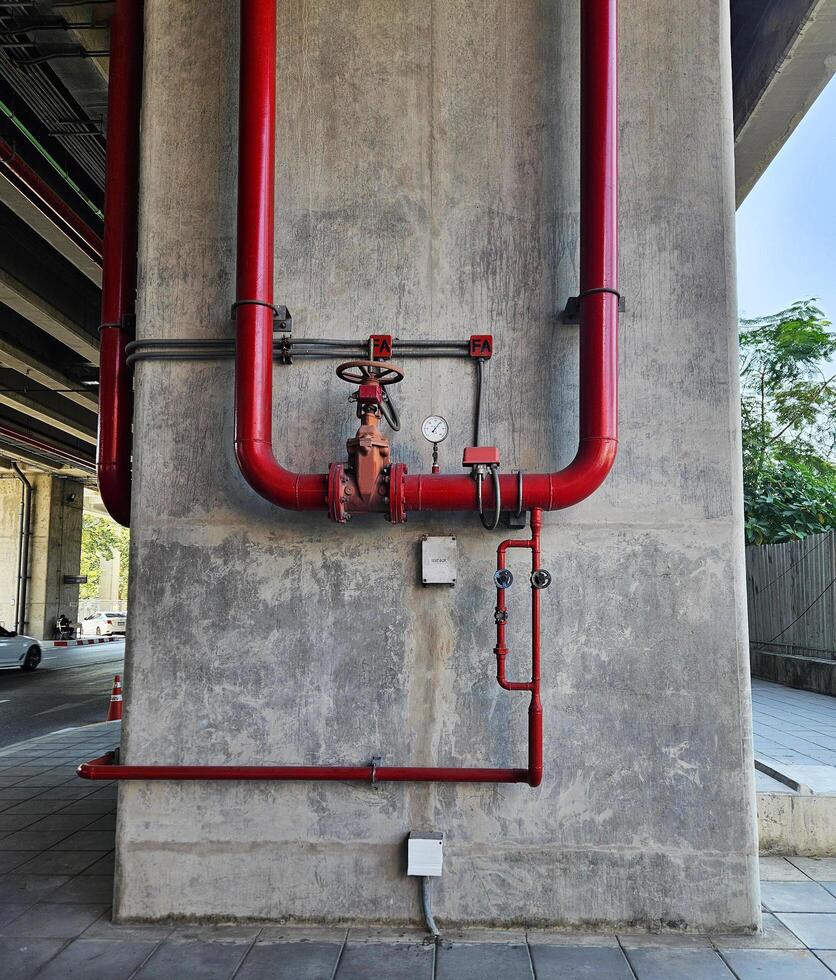 Red water or gas pipeline with gate pressure valve and stainless steel test box installed on concrete wall with copy space. Pipe industrial and extinguisher pump photo