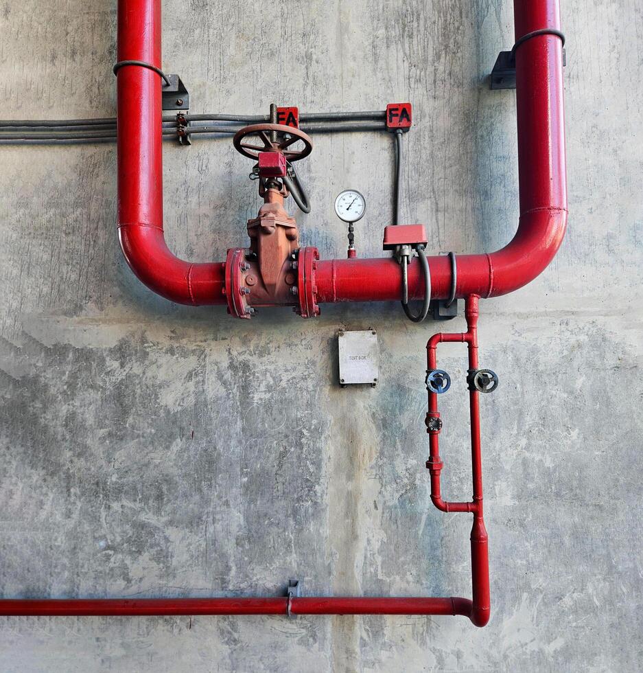 Red water or gas pipeline with gate pressure valve and stainless steel test box installed on concrete wall with copy space. Line pipe industrial and extinguisher pump photo